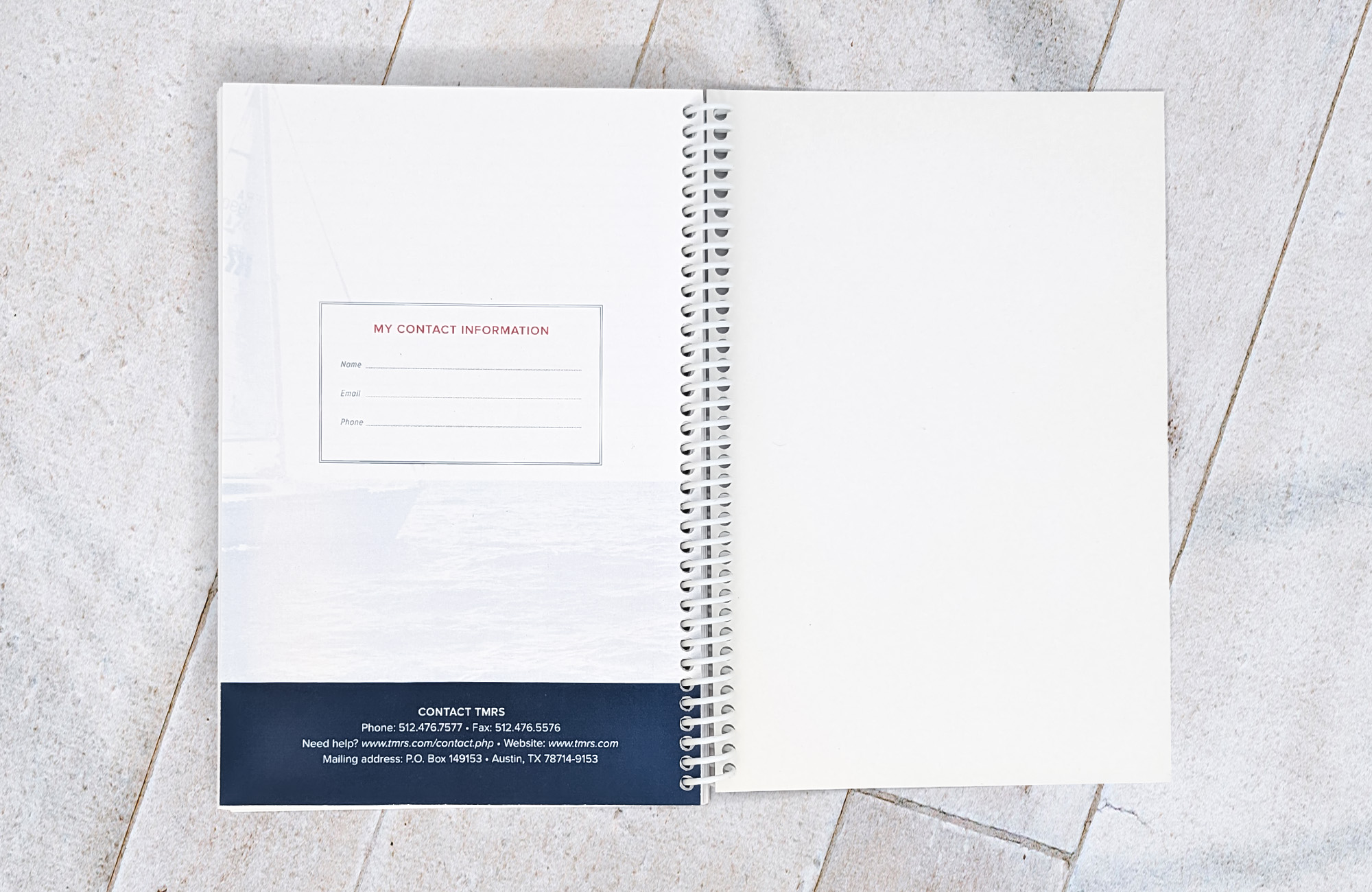 A coil-bound planner opened up to a page for personal contact information. There is a screened back image of a sailboat on the water in the background.