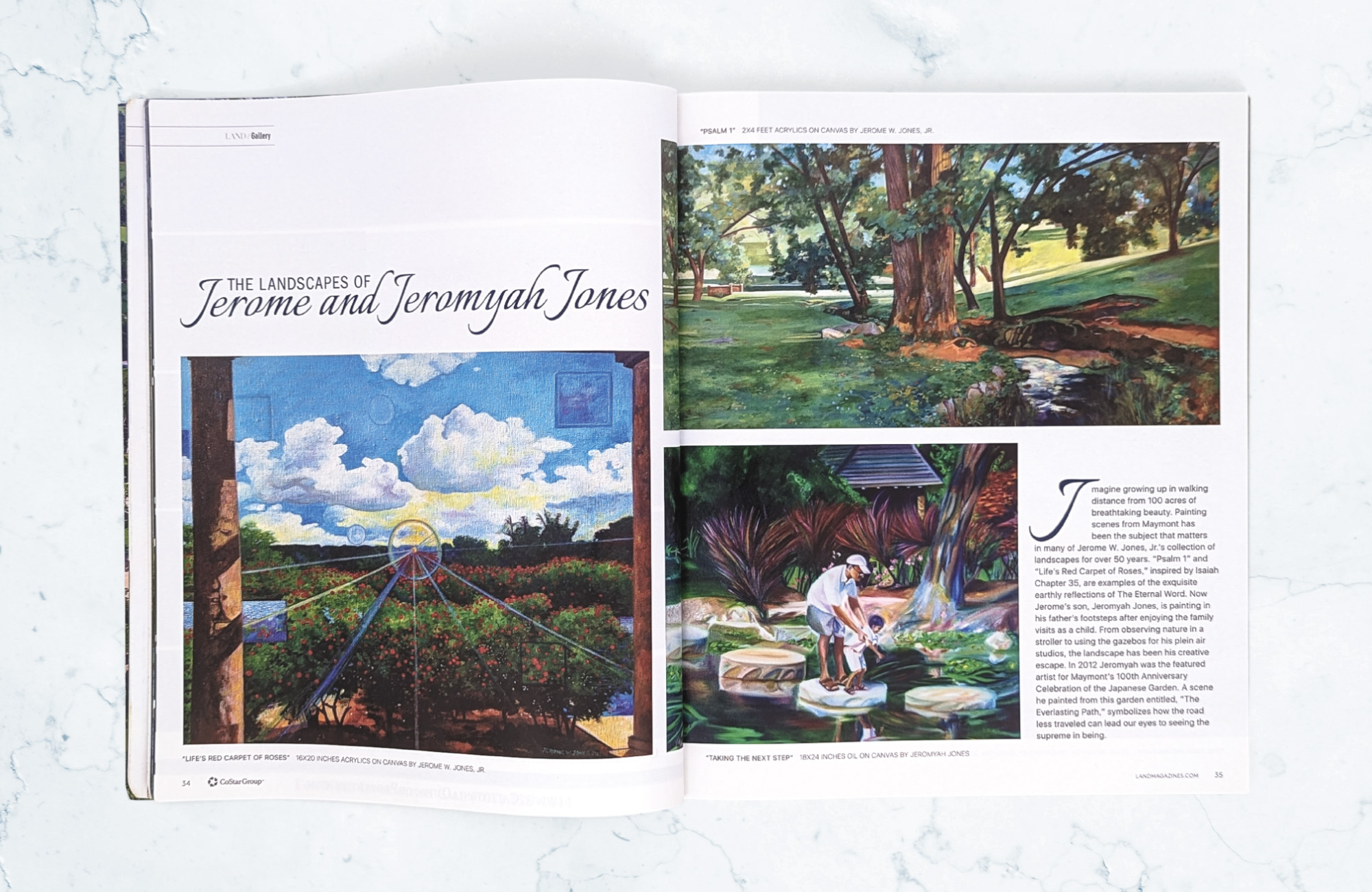 A magazine on a light marbled surface open to an editorial spread titled The Landscapes of Jerome and Jeromyha Jones. On the left is a landscape of trees with red flowers and a solar flare in the middle of the canvas. The top right has a landscape of a cluster of trees at the end of a small body of water. In the bottom right is a painting of a man holding his son as they stand on large stones in the middle of a lake.