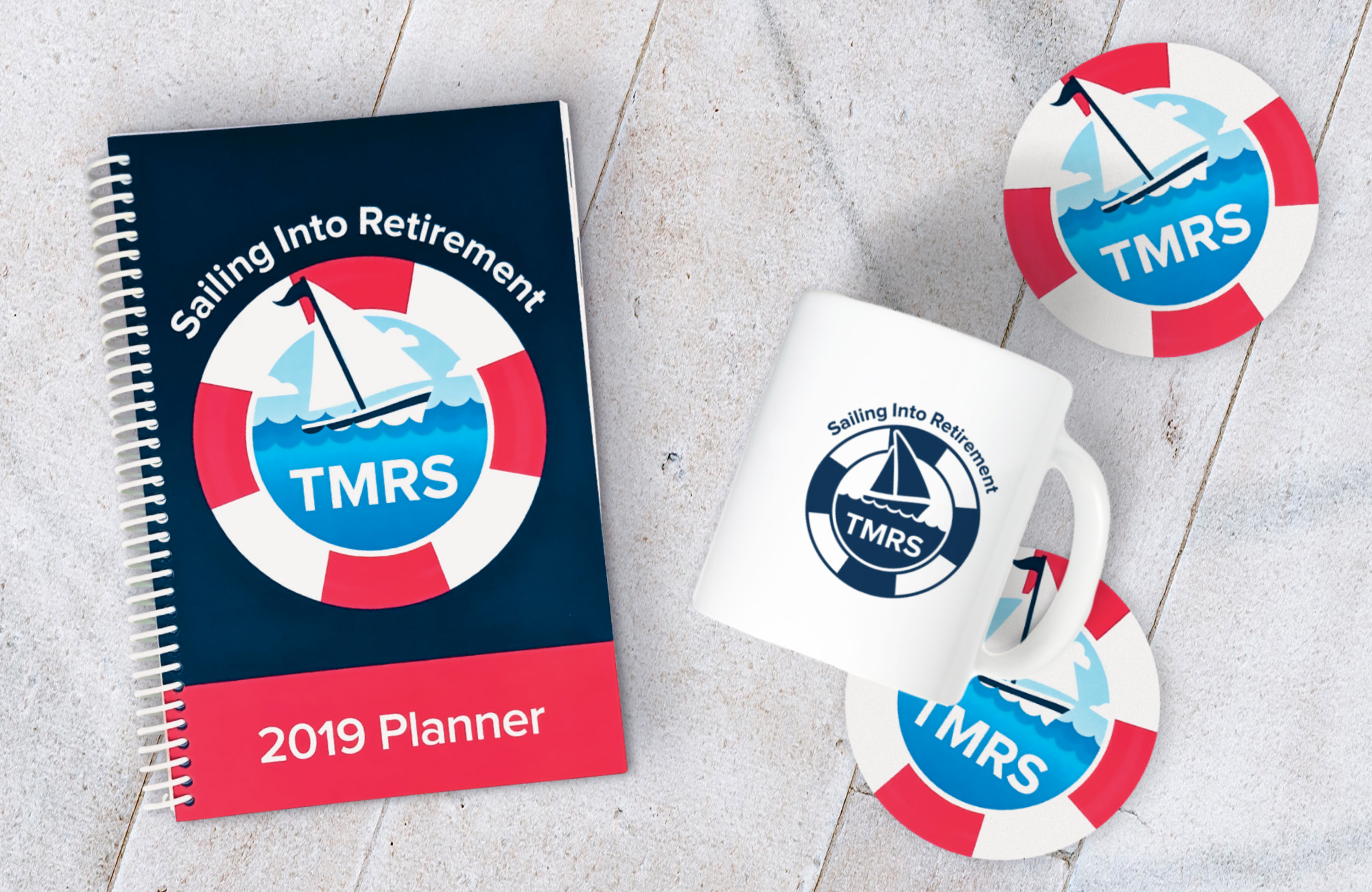 A 2019 coil-bound planner with a graphic resembling a sailboat encircled by a life preserver on the cover. To the left is a white coffee cup with the same sailboat logo. Two  round coasters featuring the same graphic are to the left of the cup.