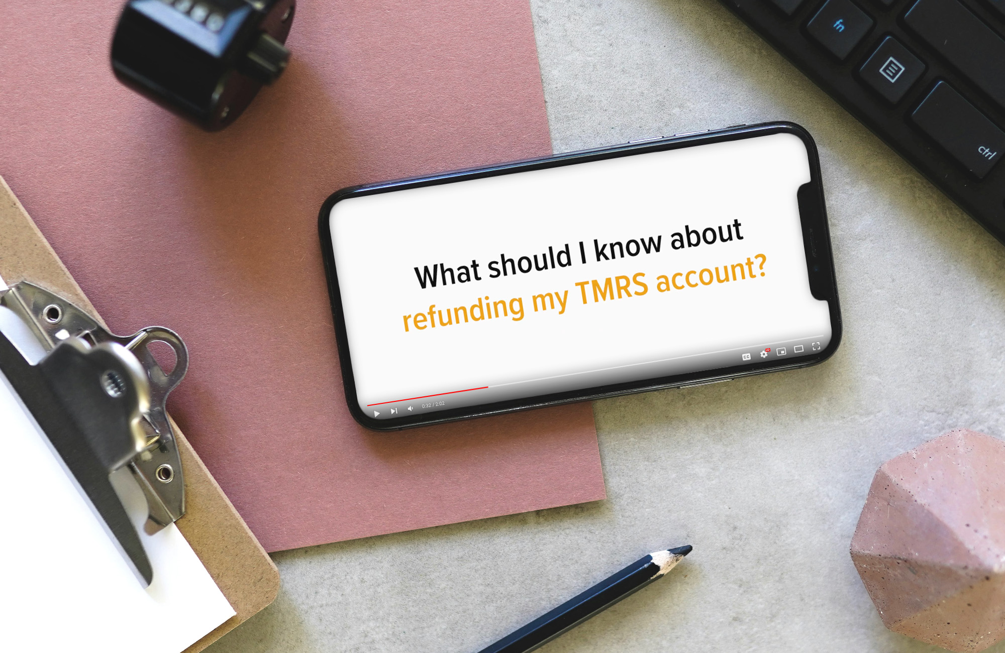 A phone is playing a youtube video on top of a cluttered desk. The screen is paused on a title card that reads: What should I know about refunding my TMRS account? class=